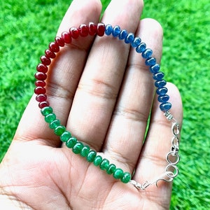 May include: A beaded bracelet featuring a gradient of colors: red, green, and blue. The bracelet is made of small, round beads and has a silver clasp. The beads are strung together to form a flexible band.