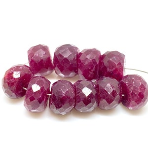 Peut inclure: Un fil de perles de rubis rouge foncé facettées. Chaque perle présente une surface géométrique à multiples facettes, captant la lumière. Les perles sont enfilées sur un fil fin de couleur argentée, parfait pour la création de bijoux.