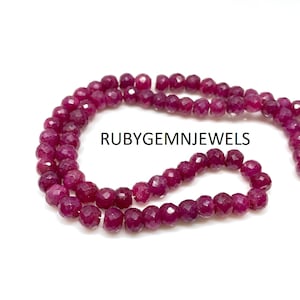 May include: Strands of faceted, deep red ruby beads. The beads are strung together, creating a necklace or bracelet. The text "RUBYGEMNJEWELS" is printed in black.