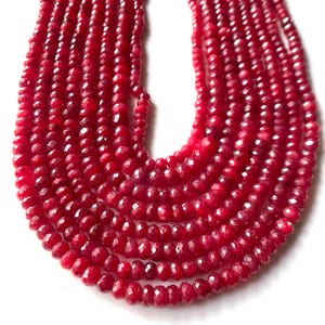 May include: A close-up of multiple strands of faceted, deep red gemstone beads. The beads are strung together, creating a layered effect. The color is a rich, saturated red, with a slight sparkle from the facets.