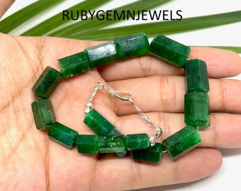 May include: A green gemstone bracelet with rectangular, faceted beads. The bracelet is strung on a silver chain with a clasp. The text "RUBYGEMNJEWELS" is visible in the image.