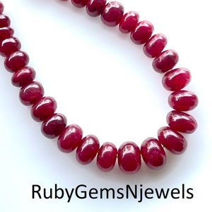 May include: A strand of polished, oval-shaped ruby beads. The beads are a deep, rich red color and appear to be strung together. The text "RubyGemsNjewels" is displayed at the bottom of the image.