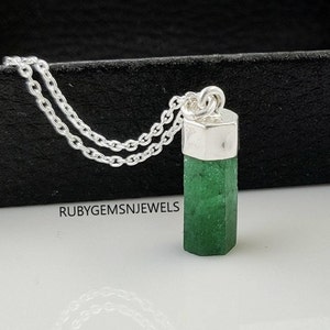 Op de afbeelding: Een zilveren ketting met een gefacetteerde, smaragdgroene edelsteen hanger. De hanger is rechthoekig met een zilveren dop. De ketting heeft een dubbele streng. De tekst "RUBYGEMSNJEWELS" is zichtbaar.