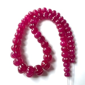 Op de afbeelding: Een streng fel magenta kralen, elk met een uitgesproken geribbelde of meloenvormige textuur. De kralen zijn in een gebogen opstelling geregen en vertonen een consistente dieproze tint en een gepolijste, reflecterende oppervlakteafwerking.