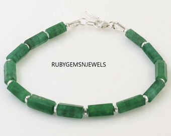 May include: A green gemstone bracelet with a silver clasp. The bracelet features multiple emerald-green, hexagonal-shaped beads. The text "RUBYGEMSNJEWELS" is visible on the image.