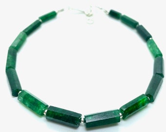 May include: A necklace featuring faceted, emerald green gemstones. The stones are strung together with small silver-colored beads and a silver clasp. The gemstones have a hexagonal shape and are a deep, rich green color.