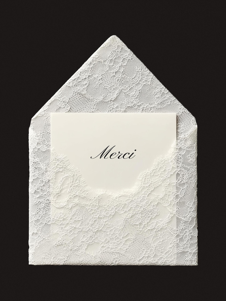 May include: A white lace envelope with a matching card inside. The card has the word "Merci" in elegant script. The envelope and card are set against a black background, highlighting the delicate lace pattern.