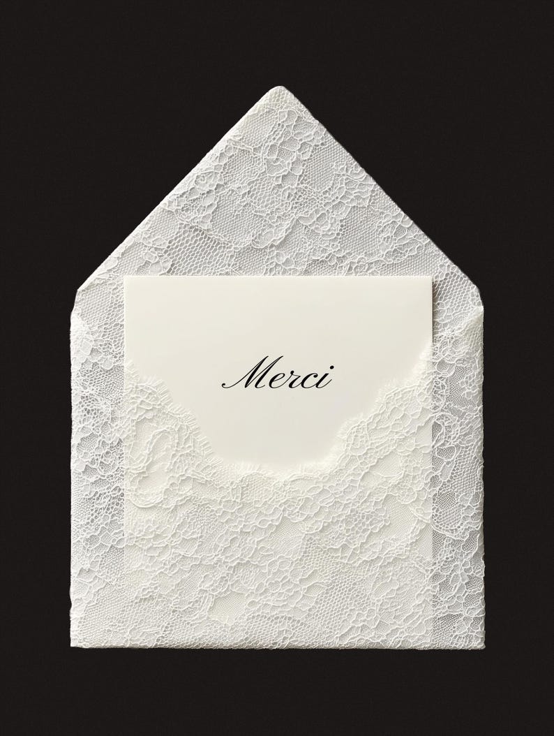 May include: A white lace envelope with a matching card inside. The card has the word "Merci" in elegant script. The envelope and card are set against a black background, highlighting the delicate lace pattern.
