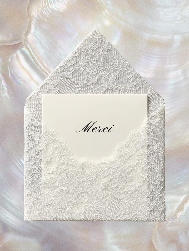 May include: A white lace envelope with a matching card inside. The card has the word "Merci" in elegant script. The envelope and card are set against a pearlescent background.