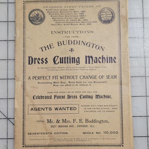 May include: A vintage paper advertisement for "The Buddington Dress Cutting Machine." The tan paper features ornate text and illustrations, including the text "Agents Wanted." The advertisement highlights awards and instructions for use.