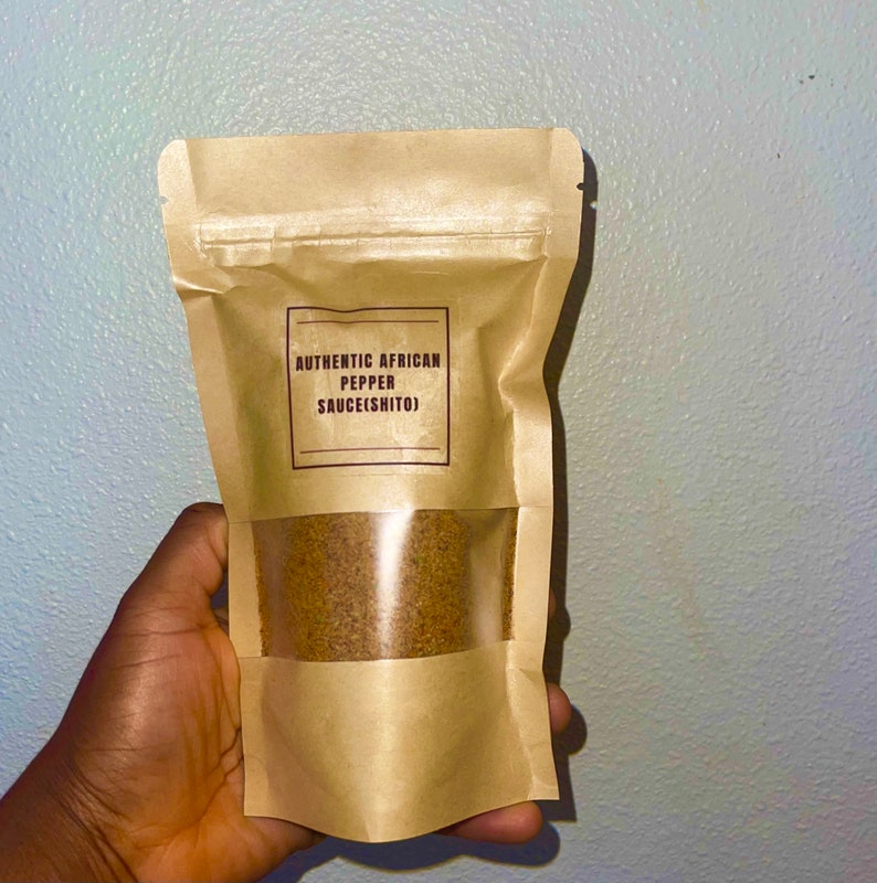 Peut inclure: Un sac en papier brun avec une fen&ecirc;tre transparente montrant une poudre brune &agrave; l'int&eacute;rieur. Le sac porte une &eacute;tiquette indiquant "AUTHENTIC AFRICAN PEPPER SAUCE(SHITO)"