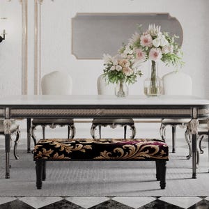 Puede incluir: Un lujoso comedor con una mesa con tapa de mármol y patas ornamentadas, rodeada de sillas tapizadas. Un banco con un cojín estampado se encuentra debajo de la mesa. Un jarrón de flores y un espejo adornan la pared, creando un ambiente elegante.