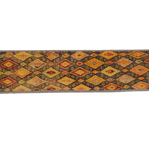 May include: A long, narrow rug with a geometric pattern in shades of orange, yellow, red, and black. The rug has a gray border.