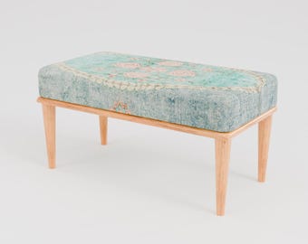 May include: A light blue and beige patterned bench with wooden legs. The bench is made of wood and fabric.