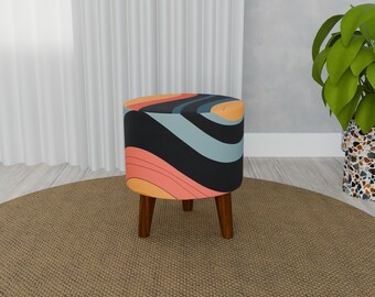 Puede incluir: Un puf redondo de color negro y blanco con patas de madera. El puf tiene un diseño abstracto colorido con tonos de azul, naranja y rosa.
