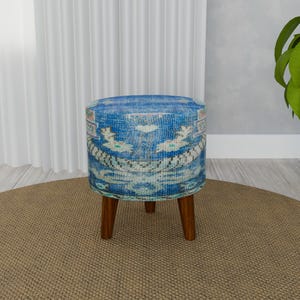 May include: A blue and white patterned ottoman with four wooden legs. The ottoman is sitting on a brown rug.