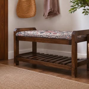 A wooden bench with a floral patterned seat sits in a room with a woven basket and a potted plant.