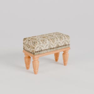 May include: A small, rectangular footstool with a beige and brown patterned fabric top and four wooden legs.