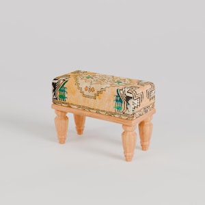 May include: A small wooden stool with four legs and a rectangular top covered in a patterned fabric with green, black, and white designs.