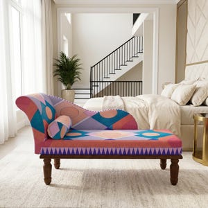 May include: A chaise lounge featuring a vibrant geometric pattern in shades of pink, orange, purple, and blue. The piece includes a matching cylindrical bolster pillow, a curved backrest, and dark brown wooden legs with a turned design.