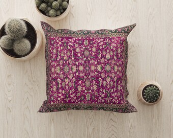 Op de afbeelding: Een roze en groen gepatroneerd kussen met een donkergroene rand. Het kussen ligt op een licht houten oppervlak met twee kleine potcactussen.