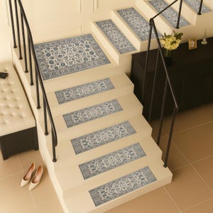 Può includere: Una scala con gradini beige e ringhiera nera. Ogni gradino ha un tappeto rettangolare con un motivo floreale blu e bianco. Un tappeto più grande con lo stesso motivo è sull'atterraggio. Tacchi alti beige sono alla base delle scale.