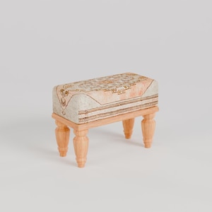 May include: A small, wooden stool with a light brown, patterned cushion. The stool has four legs and is made of wood.