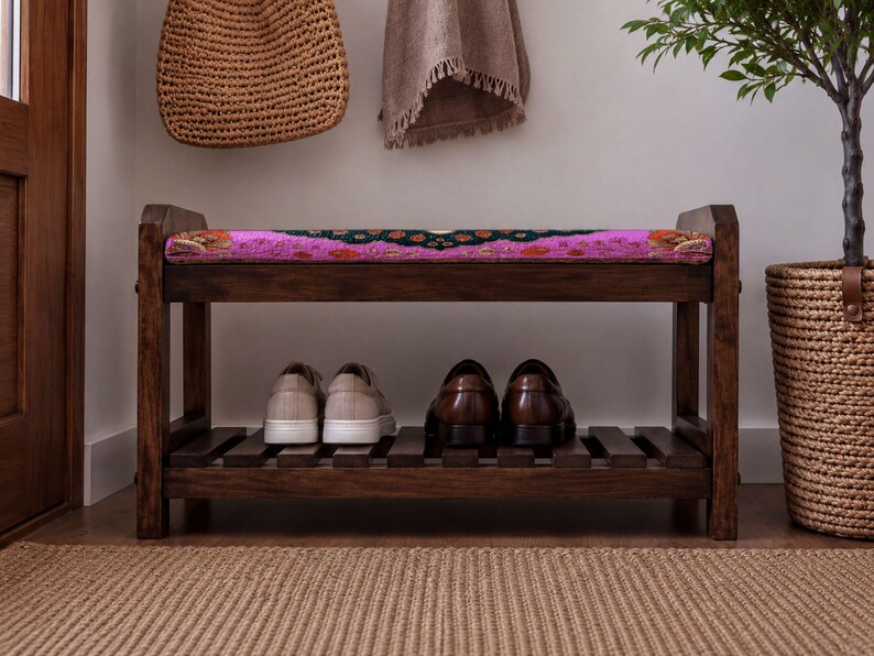 A wooden bench with a colorful cushion sits in a hallway, holding a pair of shoes on its lower shelf.