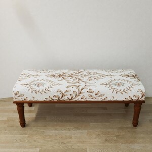 May include: A rectangular upholstered bench with a white background and a brown floral pattern. The bench has a dark brown wooden frame and four turned legs. The bench measures approximately 36 inches long, 18 inches wide, and 18 inches high.