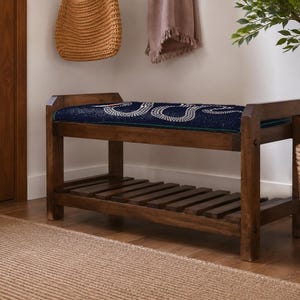 a wooden bench with a blue cushion, placed on a wooden floor next to a woven basket and a potted plant.