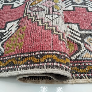 May include: Close-up of a red, white, and black patterned rug with a geometric design. The rug is folded in half, showing the texture of the fabric.