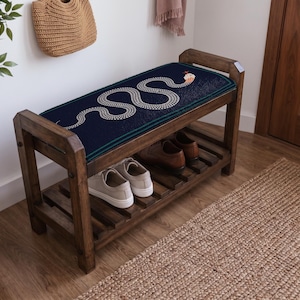 a wooden bench with a blue and white snake design on the seat, placed on a wooden floor next to a woven basket and a rug.