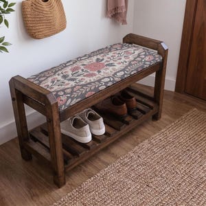 a wooden bench with a floral patterned seat and a shelf underneath, placed in a room with a woven basket and a rug on the floor.