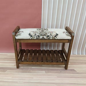 Peut inclure: Un banc en bois avec un coussin à motifs et une étagère inférieure. Le banc est brun et le coussin a un motif floral.