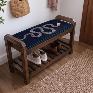 a wooden bench with a blue and white snake design on the seat, placed on a wooden floor next to a woven basket and a rug.
