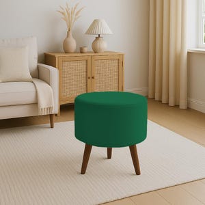 May include: A round, emerald green ottoman with three wooden legs. The upholstered seat is a solid, vibrant green. The legs are a dark brown color, providing a contrast to the green seat. This small accent furniture piece is suitable for a living room or bedroom.