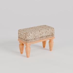 Könnte beinhalten: Ein kleiner, rechteckiger Hocker mit vier Holzbeinen und einer beigefarbenen Stoffbezug mit Blumenmuster.