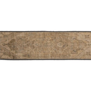May include: A long, rectangular rug with a faded, light brown color and a subtle pattern. The rug has a dark gray border.