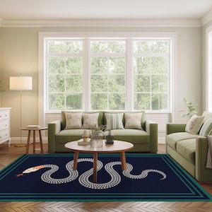 May include: A navy blue rectangular rug featuring a white snake design and a teal border. The snake has a red tongue and a pattern of white dots. The rug is in a living room with green sofas and a wooden coffee table.