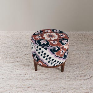 May include: A round ottoman with a floral pattern in shades of red, purple, and navy blue. The ottoman has a wooden base and legs. The fabric design features stylized flowers and leaves. The ottoman is a decorative furniture piece.
