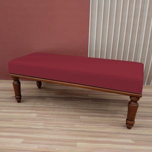 May include: A red upholstered bench with wooden legs. The bench is sitting on a wooden floor.