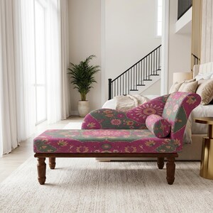 May include: A chaise lounge featuring a vibrant magenta and sage green floral pattern upholstery. The piece has a curved backrest, a matching cylindrical bolster pillow, and four dark brown wooden legs with a turned, spindle-style design.