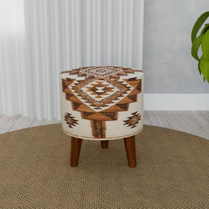 May include: A round, white and brown patterned ottoman with four wooden legs. The ottoman is sitting on a brown rug.