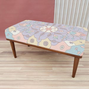 May include: A wooden bench with a colorful patterned cushion. The cushion features a geometric design with pink, blue, yellow, and white colors.