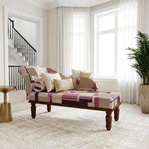 May include: A chaise lounge featuring a geometric pattern in shades of purple, pink, beige, and brown. The piece has a curved backrest, a cylindrical bolster pillow, two square throw pillows, and dark wooden legs with a turned design.