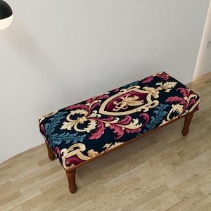 May include: A rectangular bench with a dark blue patterned top featuring a crest design with a gold eagle and ornate floral elements in red, cream, and teal. The bench has four wooden legs and a dark wood frame.