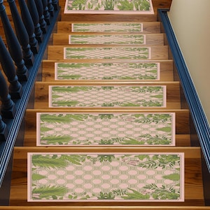 Op de afbeelding: Traptreden met een botanisch ontwerp. Elke trede heeft een lichtroze achtergrond met een groen geometrisch patroon en groene bladaccenten. Ze zijn geïnstalleerd op houten trappen met een donkerblauwe balustrade.
