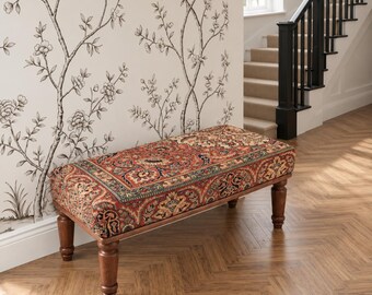 May include: A rectangular bench featuring a seat upholstered in a multi-colored fabric with a detailed red, blue, and gold floral pattern. The bench is supported by four turned wooden legs with a medium brown finish and a smooth, polished texture.
