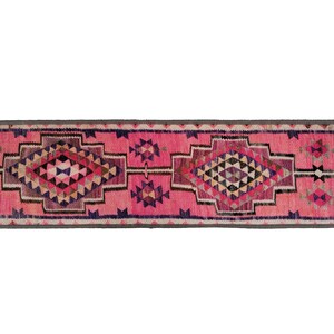 May include: A rectangular, pink runner rug with geometric patterns. The rug features diamond and triangle shapes in shades of pink, purple, black, and beige. A gray border frames the edges.