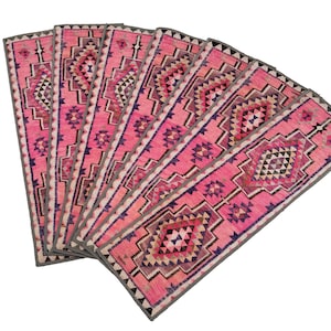 Può includere: Una collezione di tappeti runner rosa e grigi con motivi geometrici. Ogni tappeto presenta un disegno a diamante centrale con triangoli e altre forme in tonalità di rosa, viola e grigio. I bordi sono rifiniti con un bordo grigio.